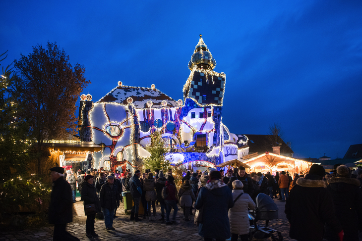 Besucher auf dem Kuchlbauer Weihnachtsmarkt vor dem beleuchteten Hundertwasser-Turm